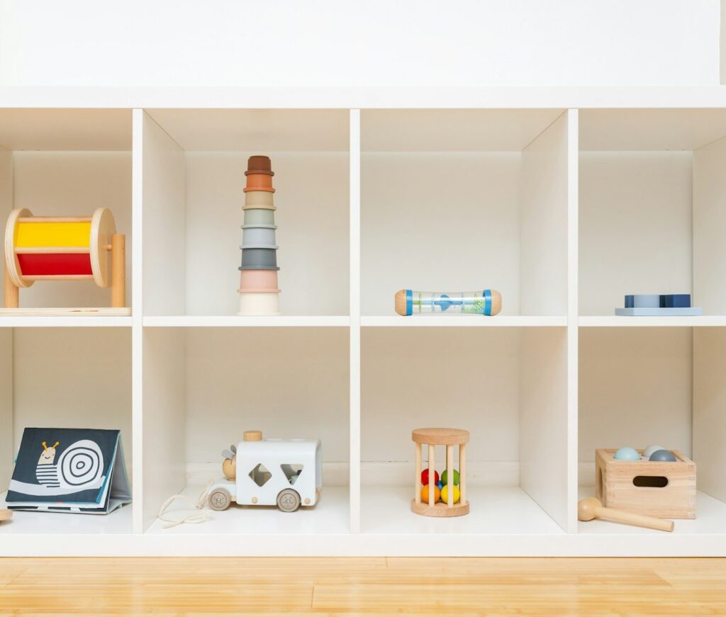 A white toy shelf with wooden baby toys, a stacking tower and a shape sorter